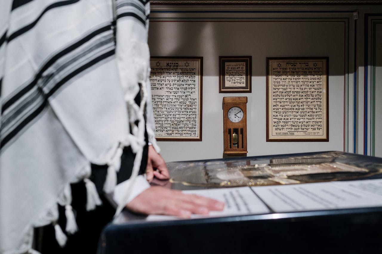 An Orthodox Jewish man engaged in prayer wearing a tallit, surrounded by traditional Hebrew scripts.